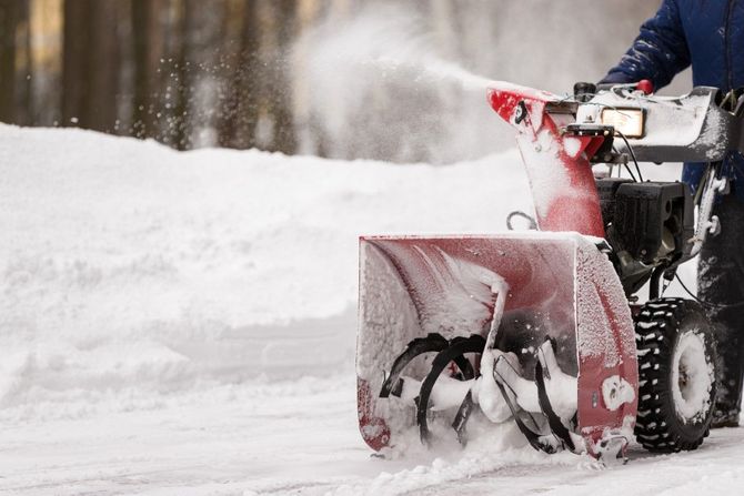 Snowblower clearing a snowy road, spraying snow from its red chute