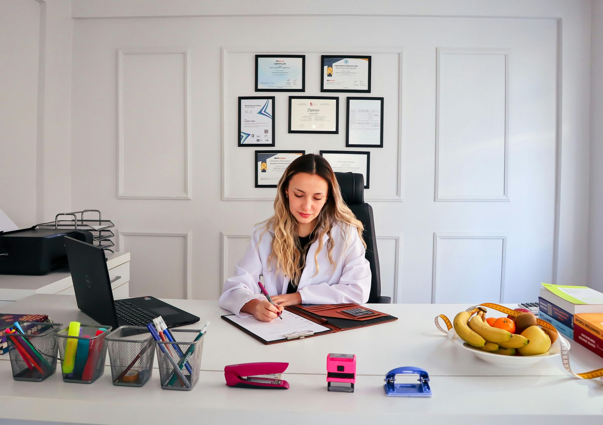 A doctor filling out paperwork with diplomas on the wall