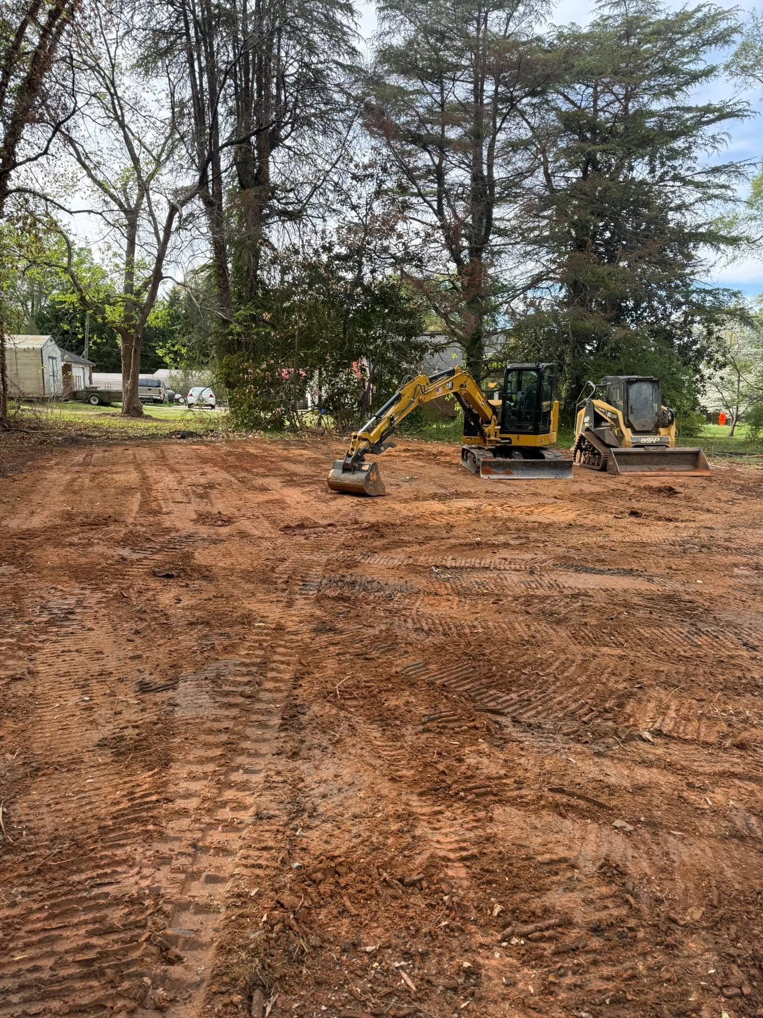 Yellow backhoe grading a dirt lot with trees in the background