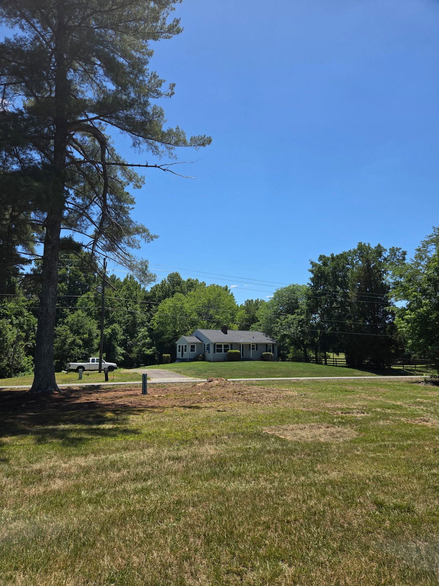 Sunny grassy yard with a small white house and trees under a clear blue sky