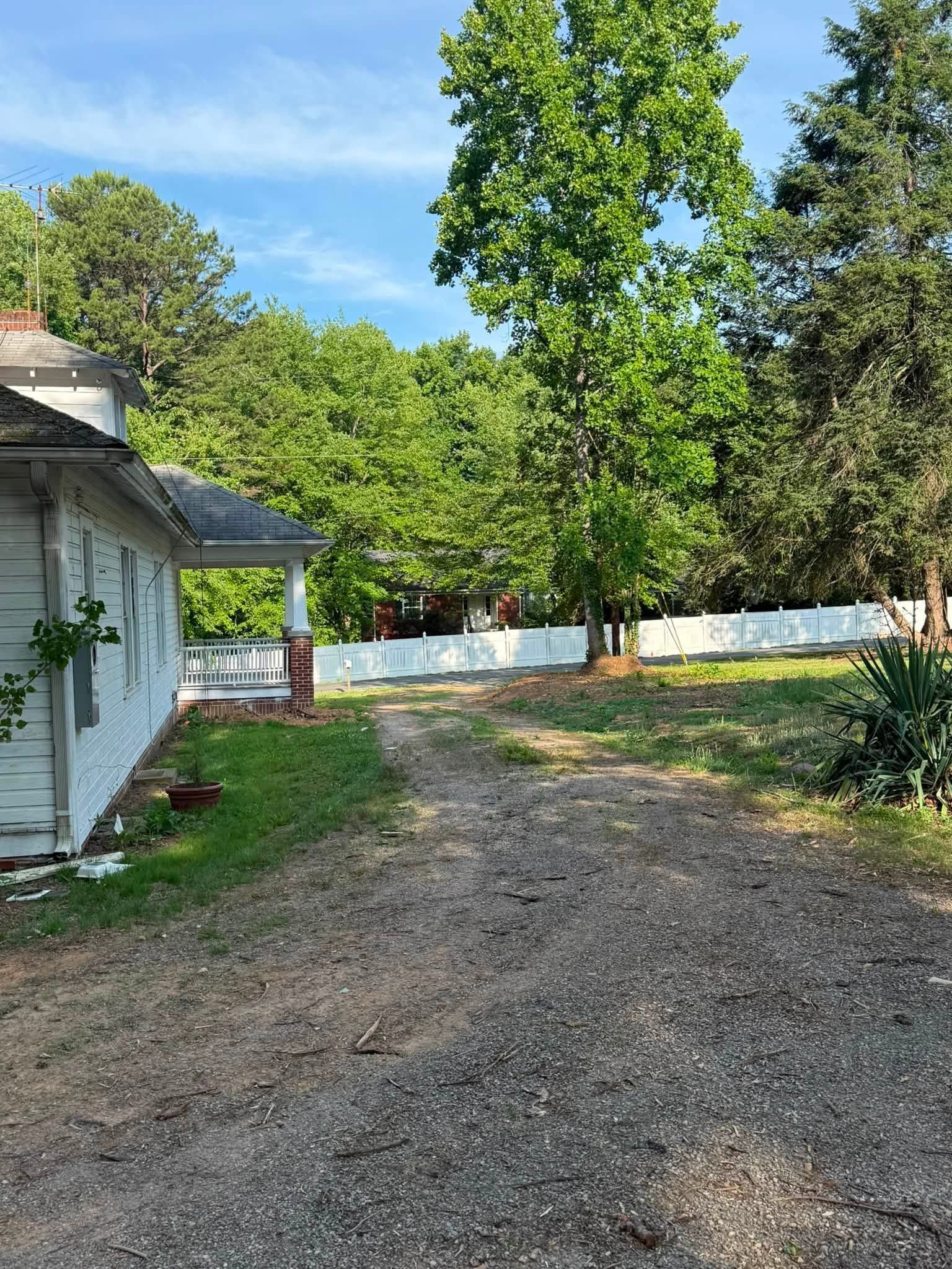 Gravel driveway beside a white house and green trees under a bright blue sky