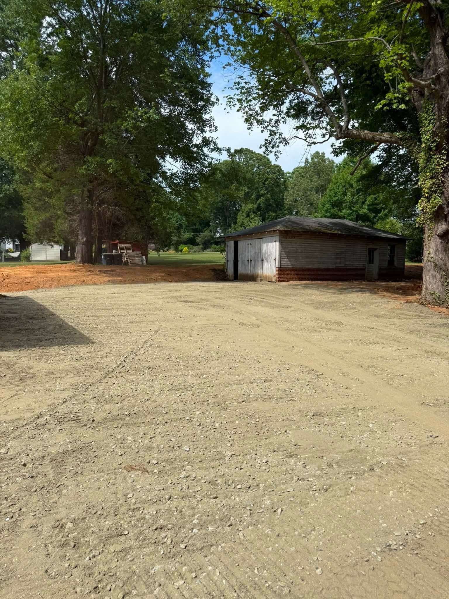 Dirt clearing with large trees and a small white building in the background
