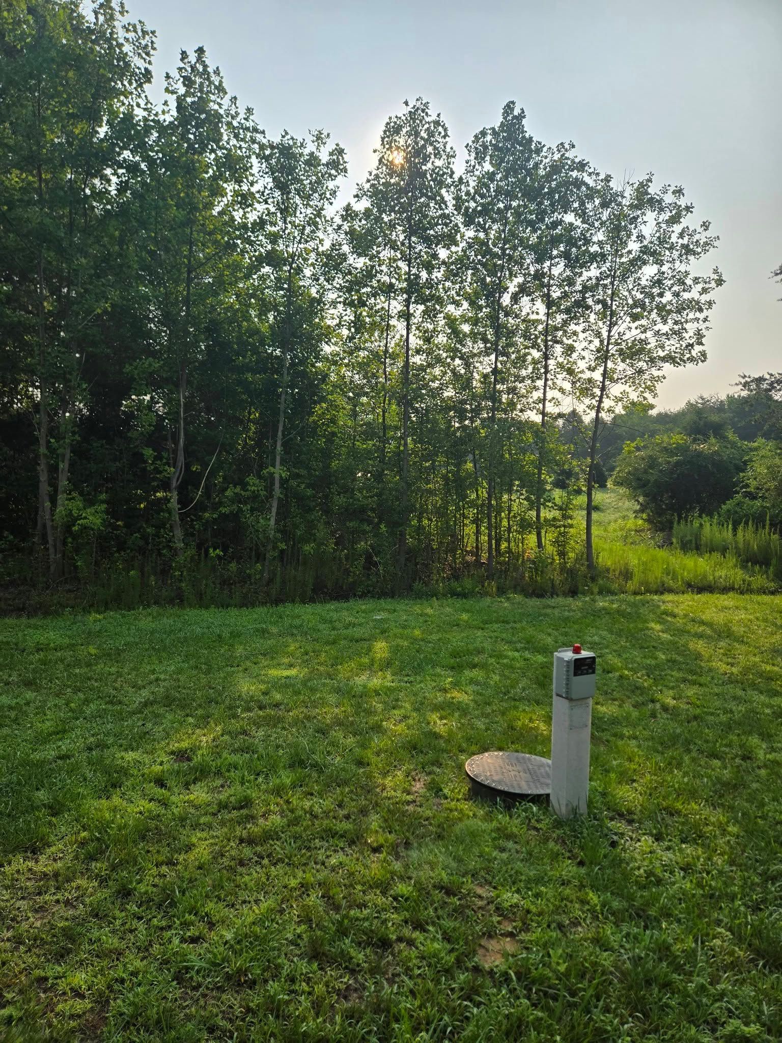 Grassy field at sunset with trees and a small white utility post in the foreground