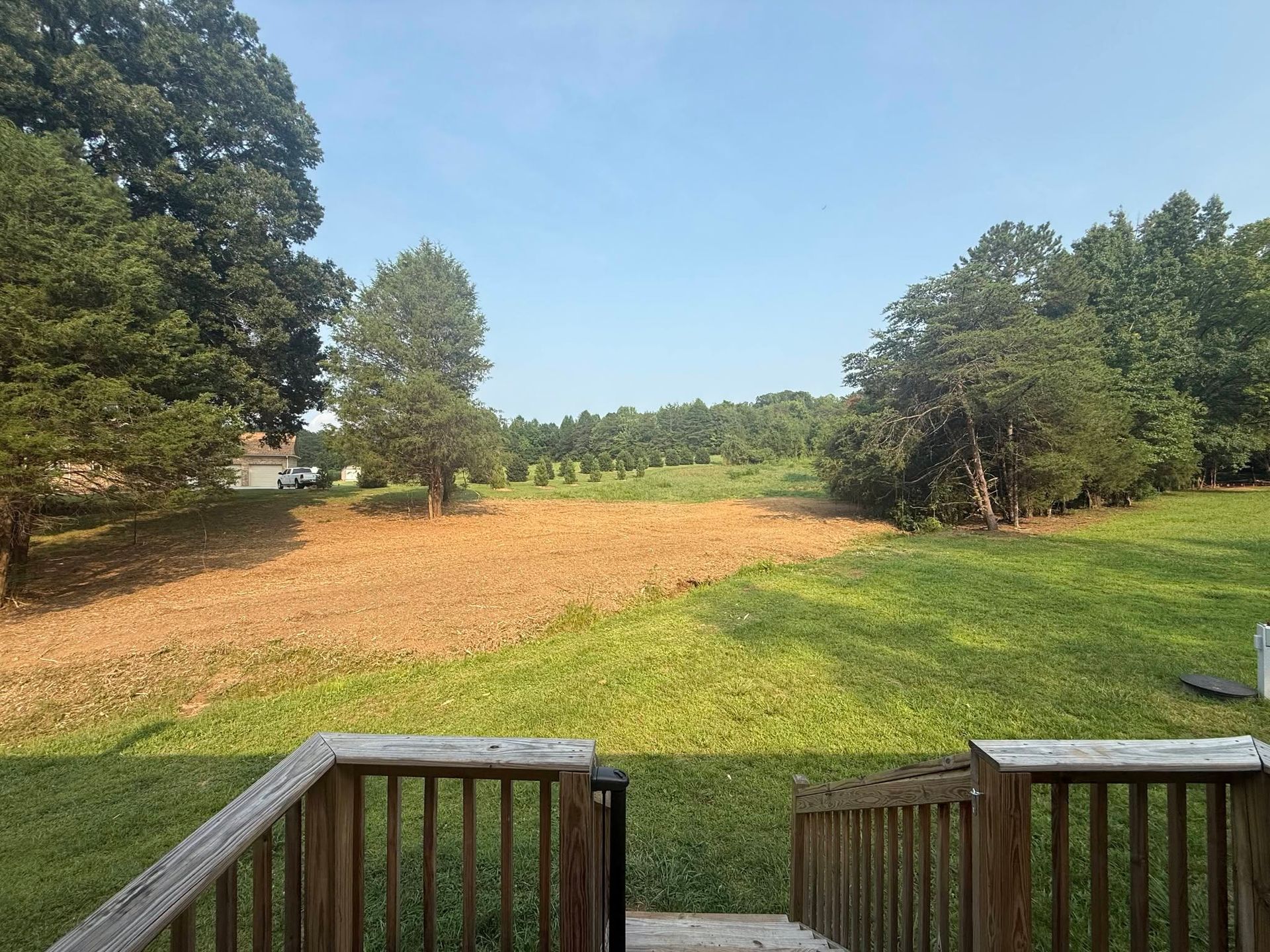 Wooden deck overlooking a grassy field with trees under a clear blue sky