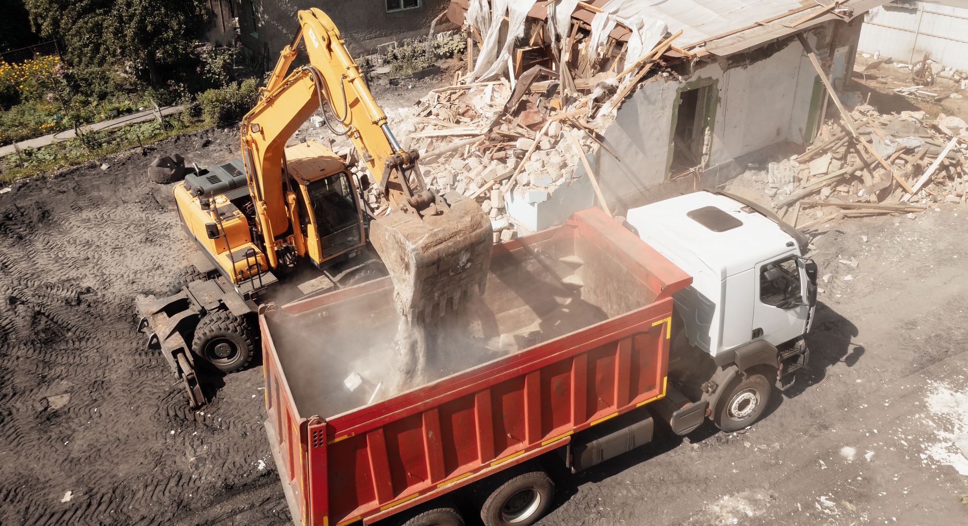 Excavator loading rubble into a red dump truck at a demolition site