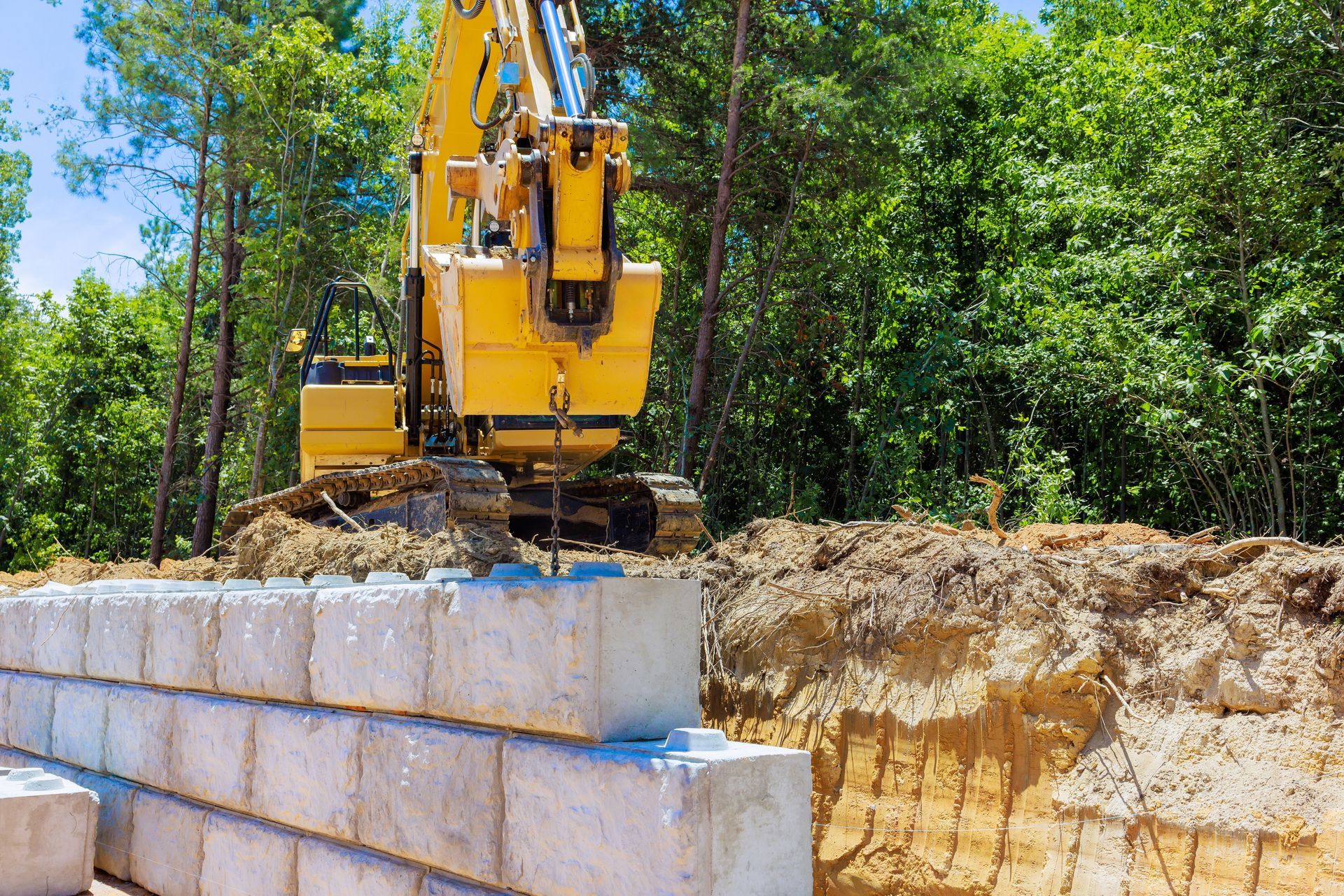 Yellow excavator building a stone retaining wall at a wooded construction site
