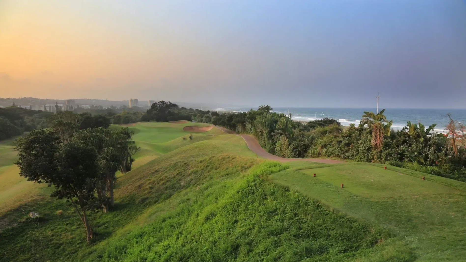 Lush green golf course hills overlooking the ocean at sunset