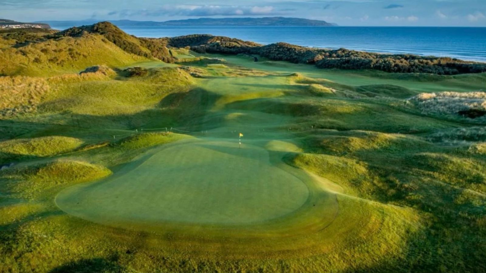 Aerial view of a green golf course beside blue ocean and rocky coastline
