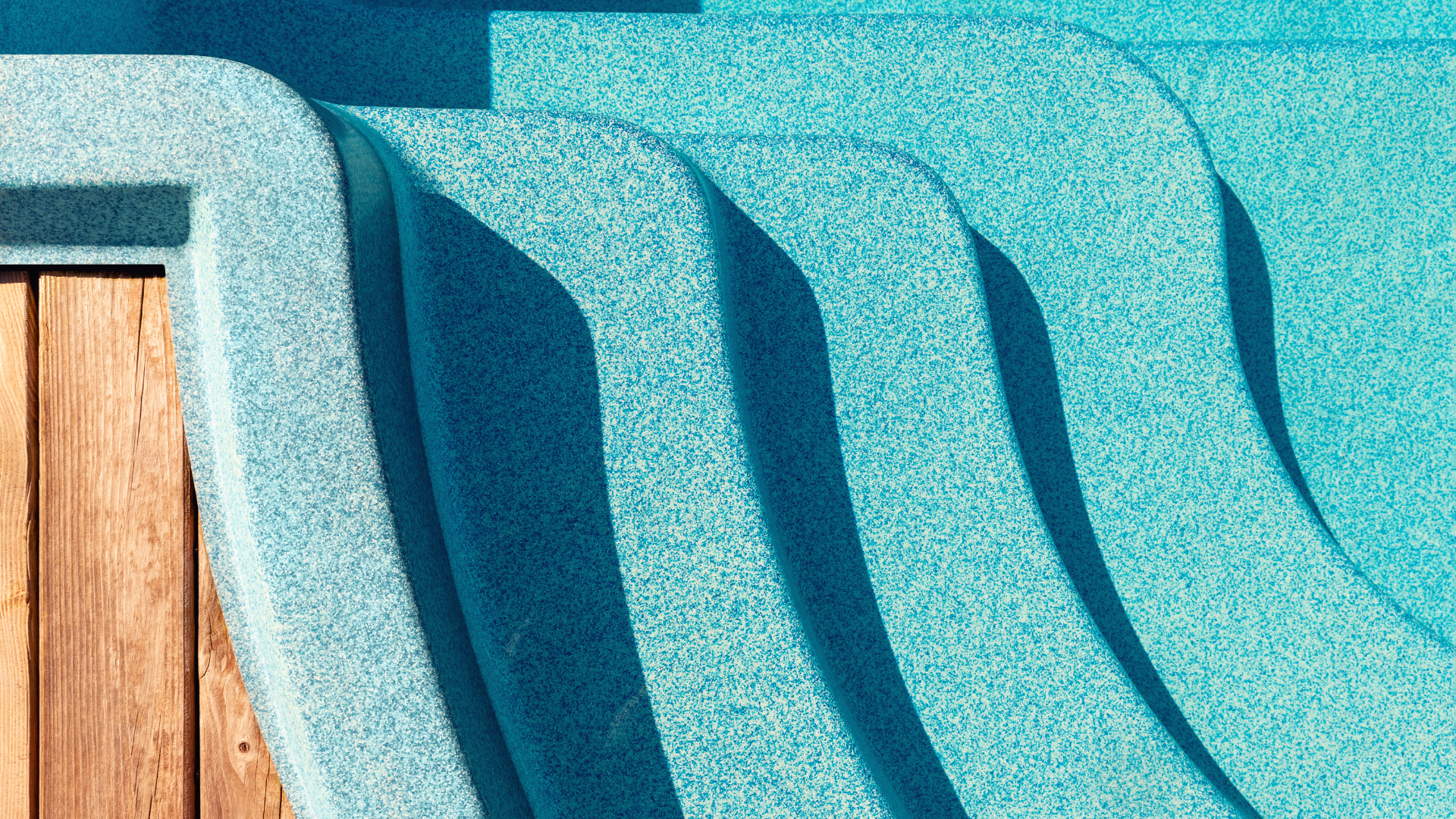 A close up of a swimming pool with stairs and a wooden deck.