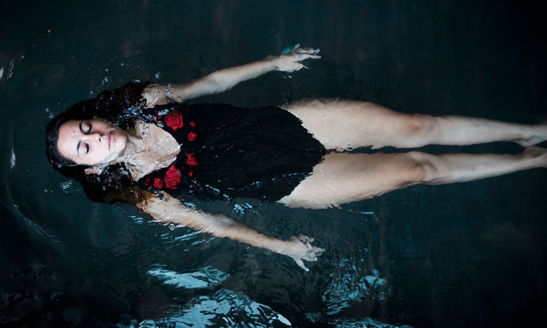 A woman in a black swimsuit is floating on her back in the water.