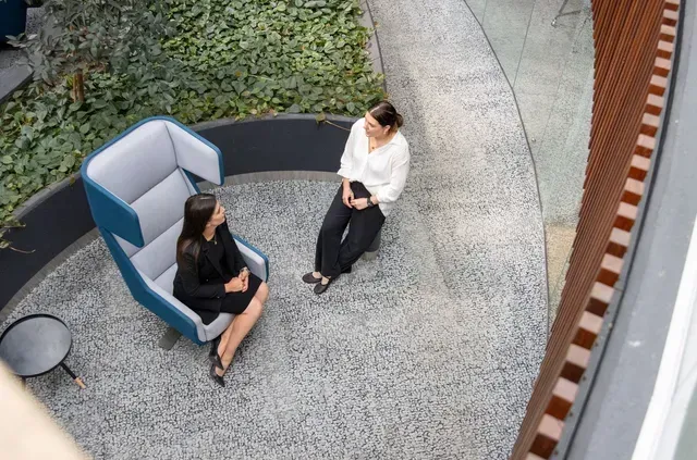Two people sitting in a curved outdoor lounge chair on a gravel patio, seen from above.