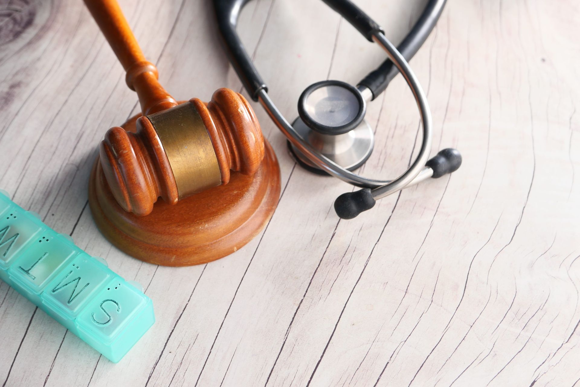 Wooden gavel and stethoscope on a light wooden table, with teal medicine pills nearby