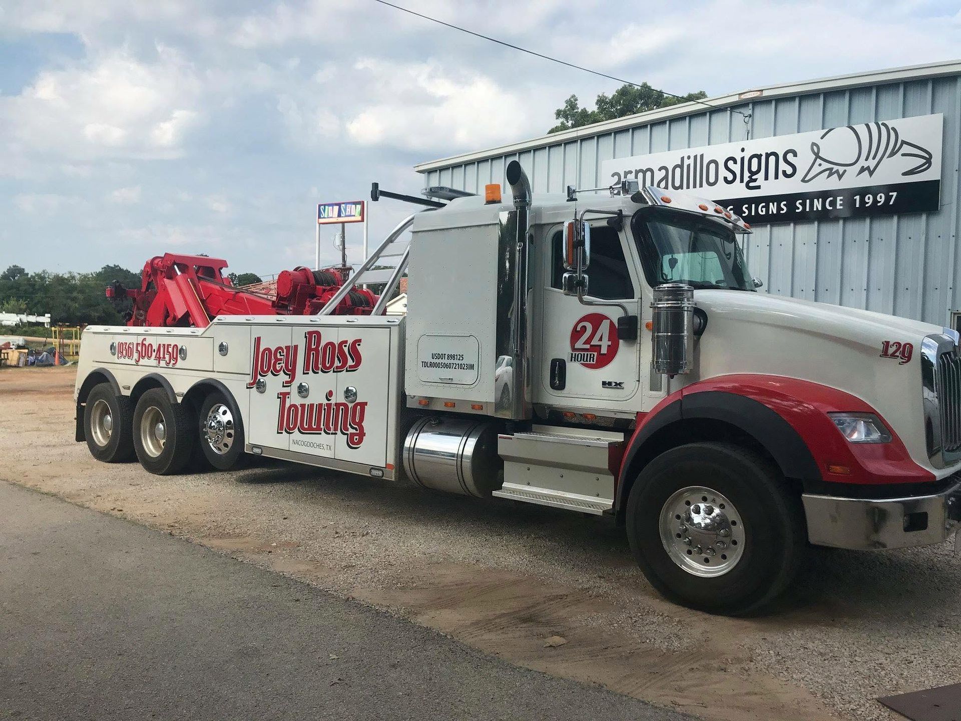Red-and-white tow truck parked beside a road with a trailer and business signage in the background