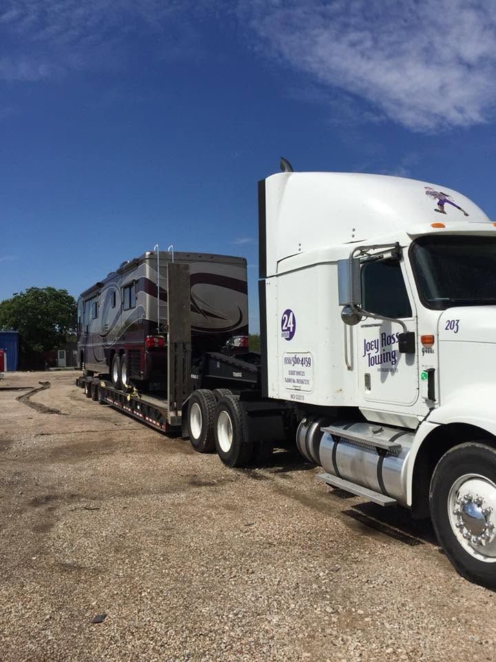 White semi-truck towing a gray RV trailer on a gravel lot under a blue sky