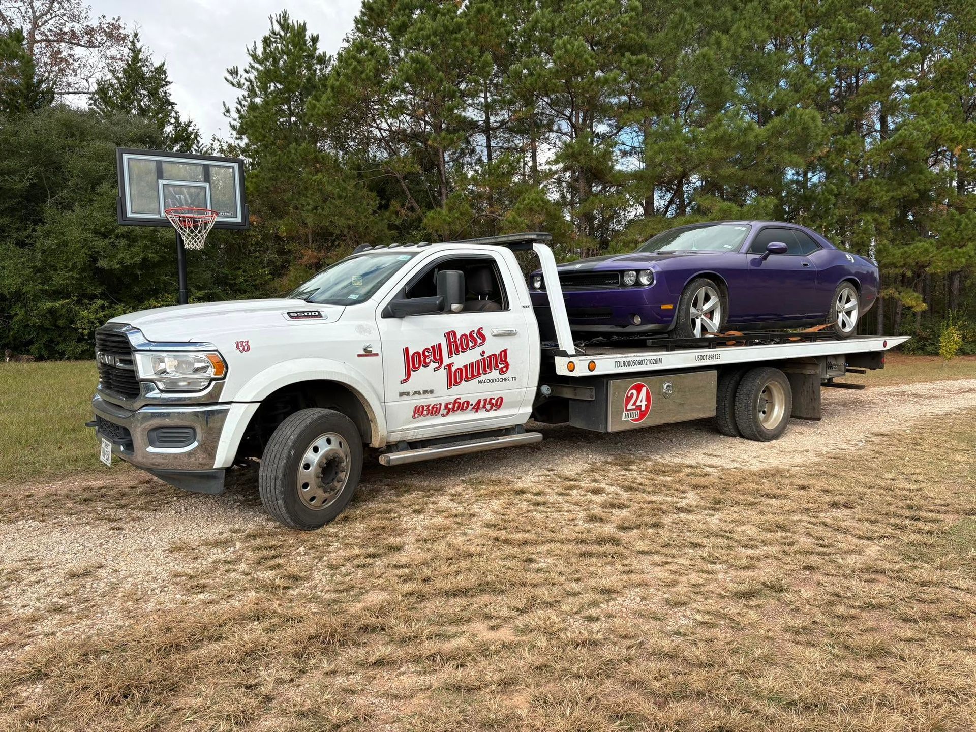 Tow truck carrying a purple car in a grassy roadside area near a basketball hoop