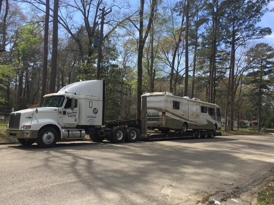 White semi-truck towing an RV on a wooded roadside in daylight