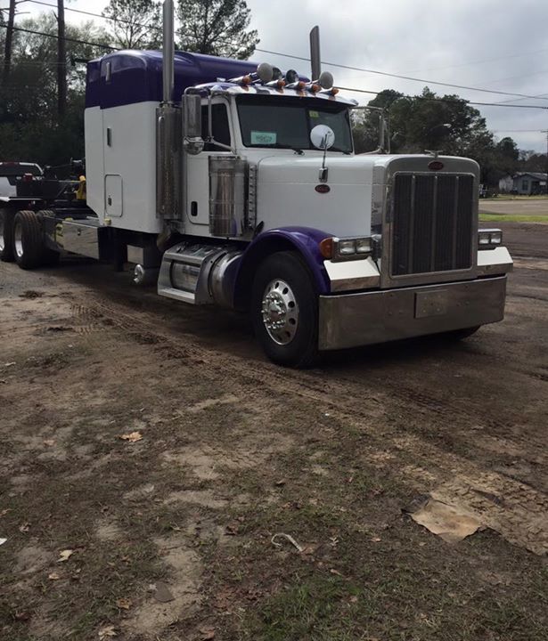 White semi-truck with purple accents parked on a dirt lot under cloudy skies