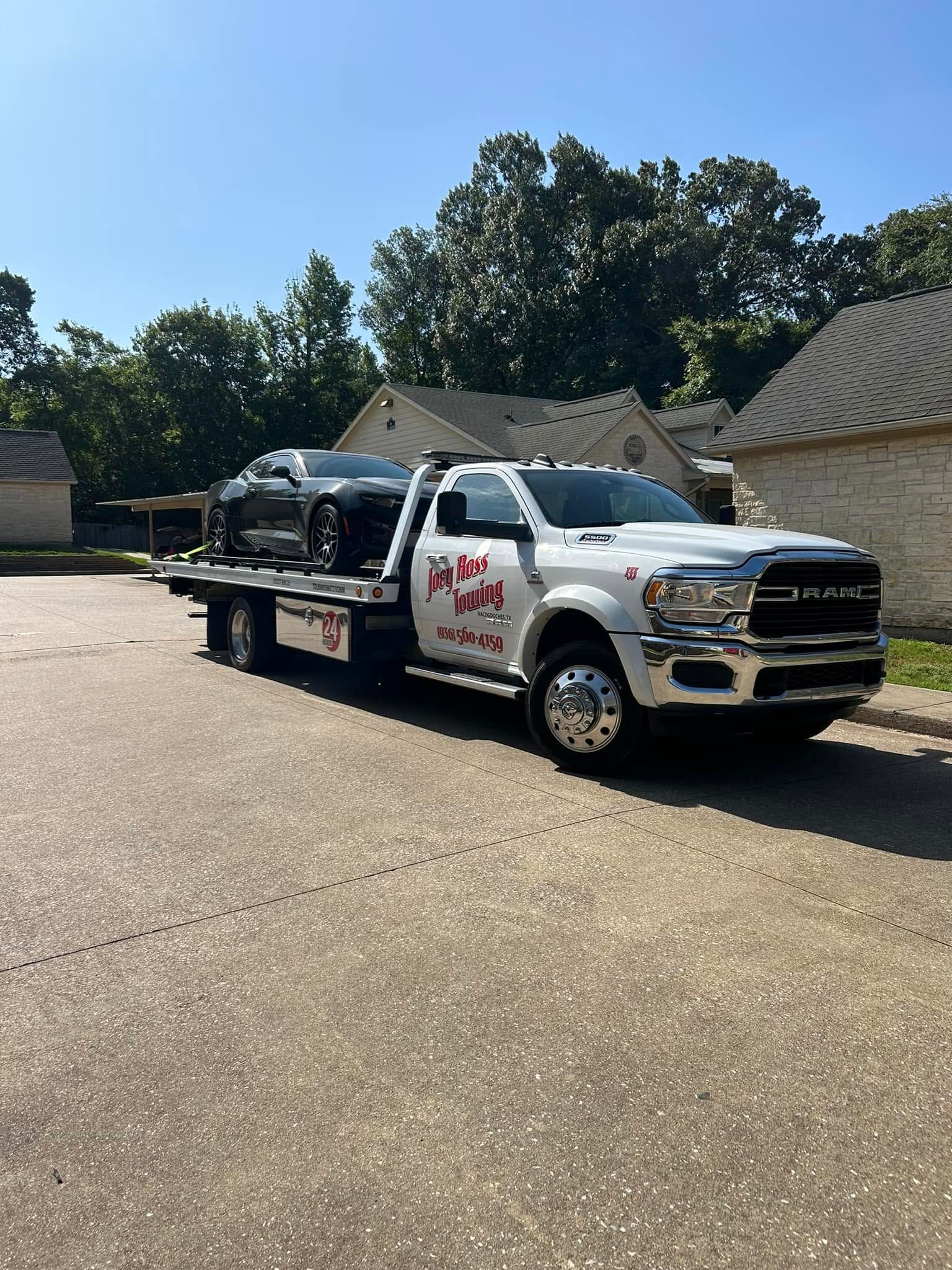 White tow truck carrying a damaged black car in a sunny parking lot