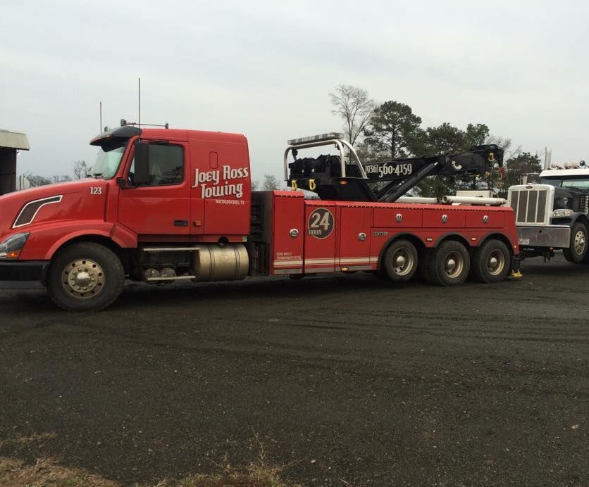 Red tow truck with flatbed trailer parked on wet pavement in an industrial lot.