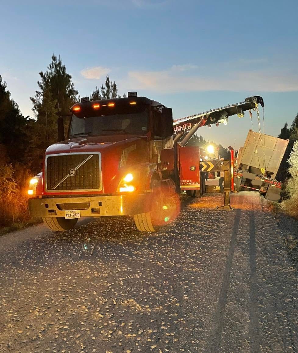 Tow truck at dusk hauling a damaged white vehicle on a rural road