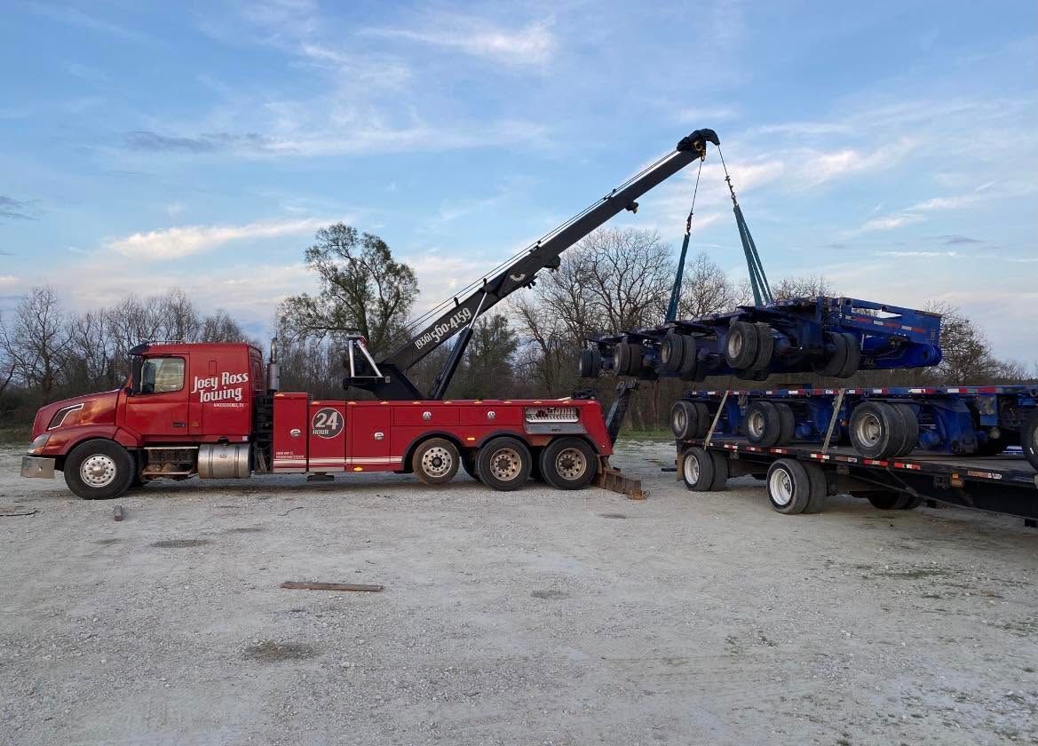 Red tow truck lifting a blue car carrier trailer loaded with vehicles in a gravel lot