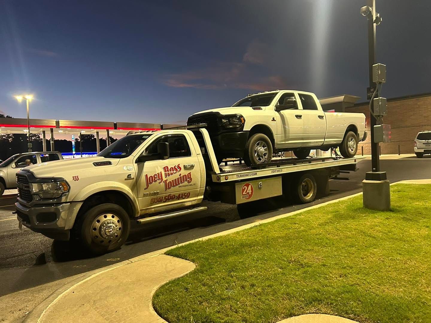 White pickup on a flatbed tow truck at dusk in a parking lot
