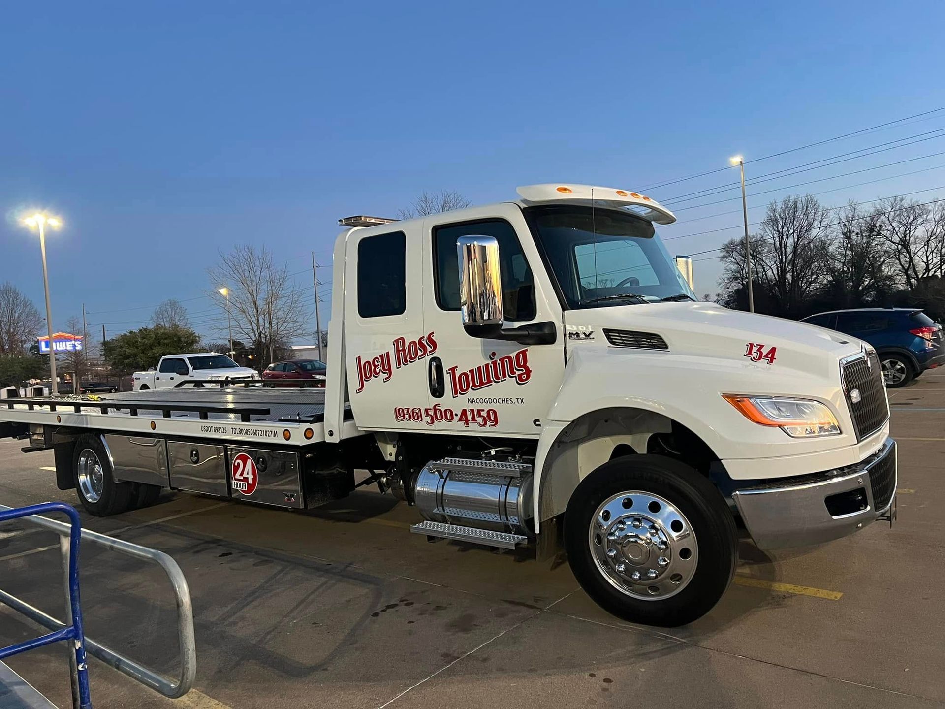 White tow truck parked outdoors at dusk with red lettering on the door and flatbed visible