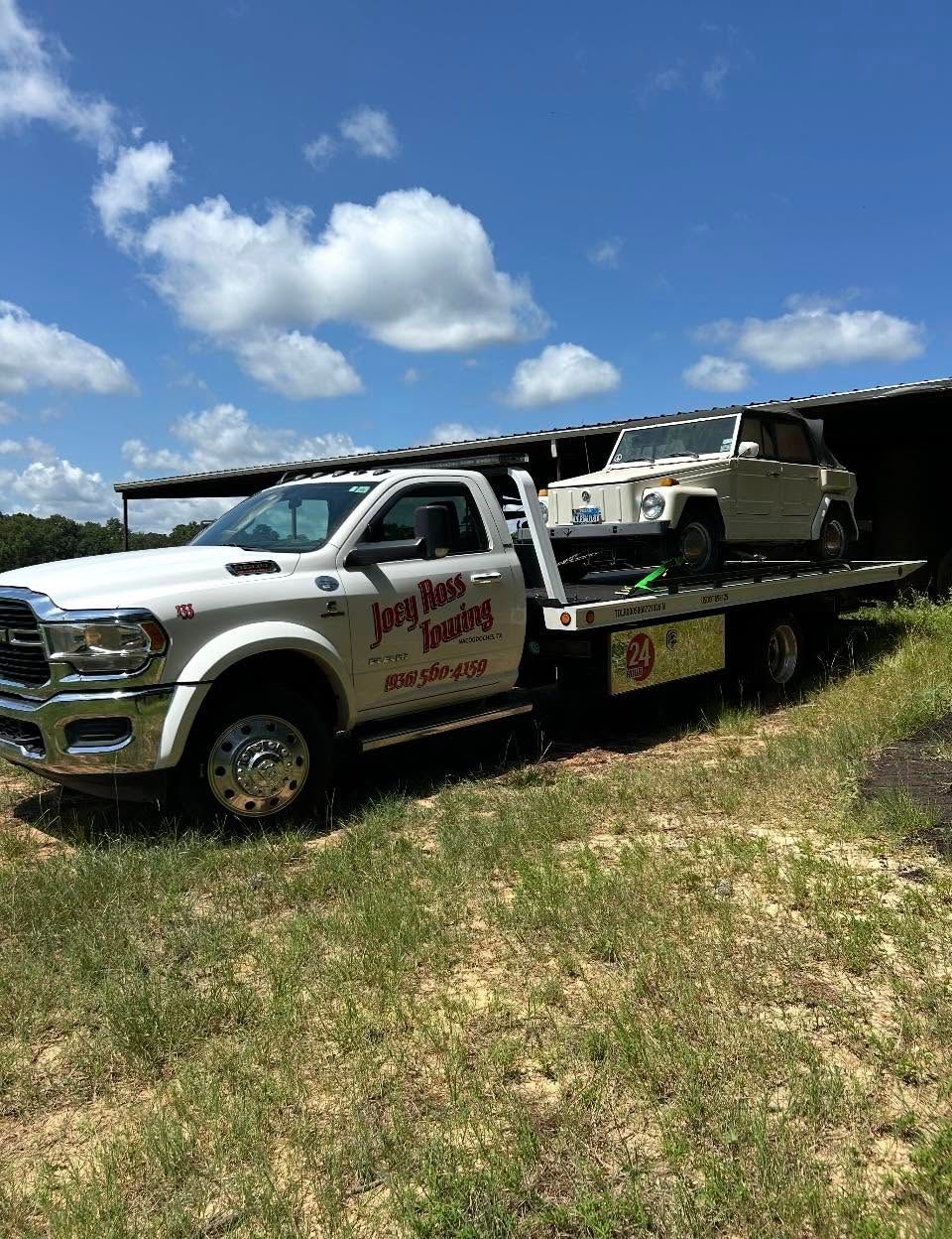 Tow truck carrying a white pickup and SUV on a flatbed under a blue sky