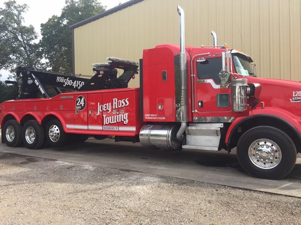 Red tow truck with “Lloyd’s Towing” parked beside a building on gravel.