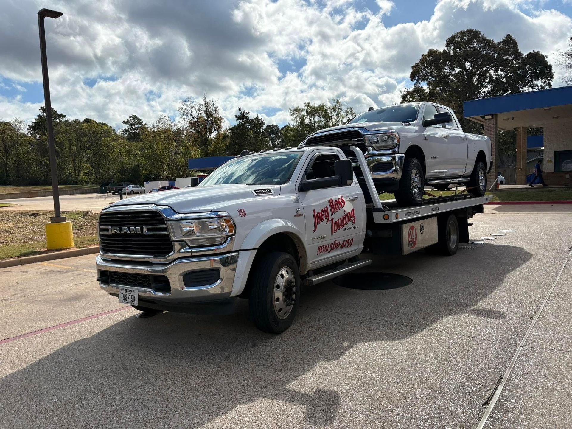 White flatbed tow truck hauling a white SUV in a parking lot under a partly cloudy sky