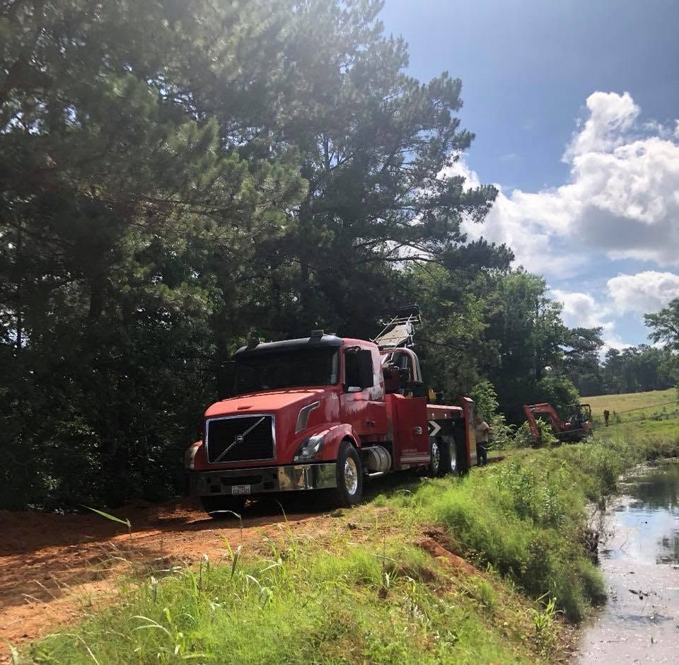 Red fire truck on a muddy roadside near a pond, with trees and a bright cloudy sky.
