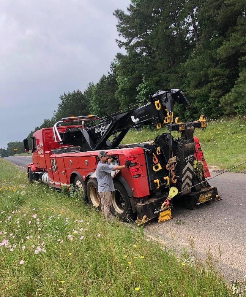 Red tow truck hauling a car on a rural road, with a person standing beside it.