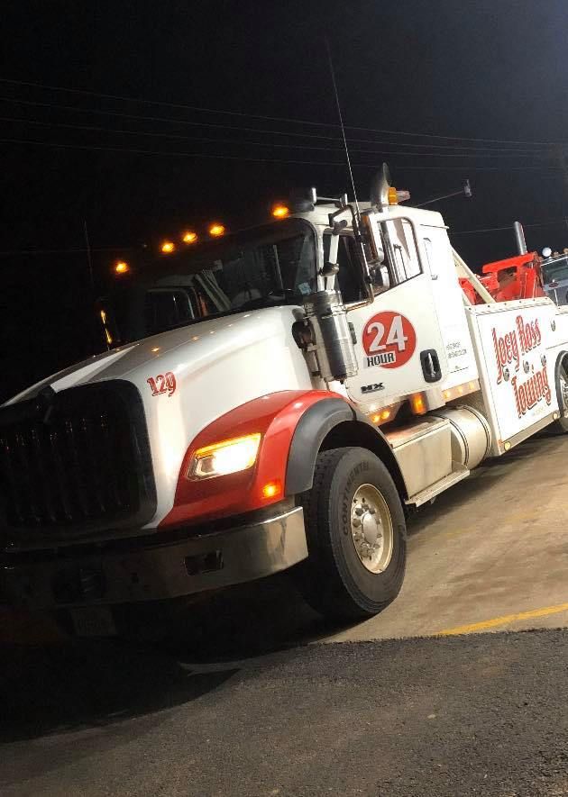 White tow truck at night, angled on a road with amber lights glowing on top.