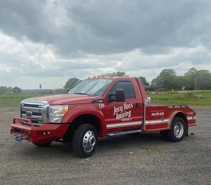 Red tow truck with white lettering parked on gravel under cloudy sky.