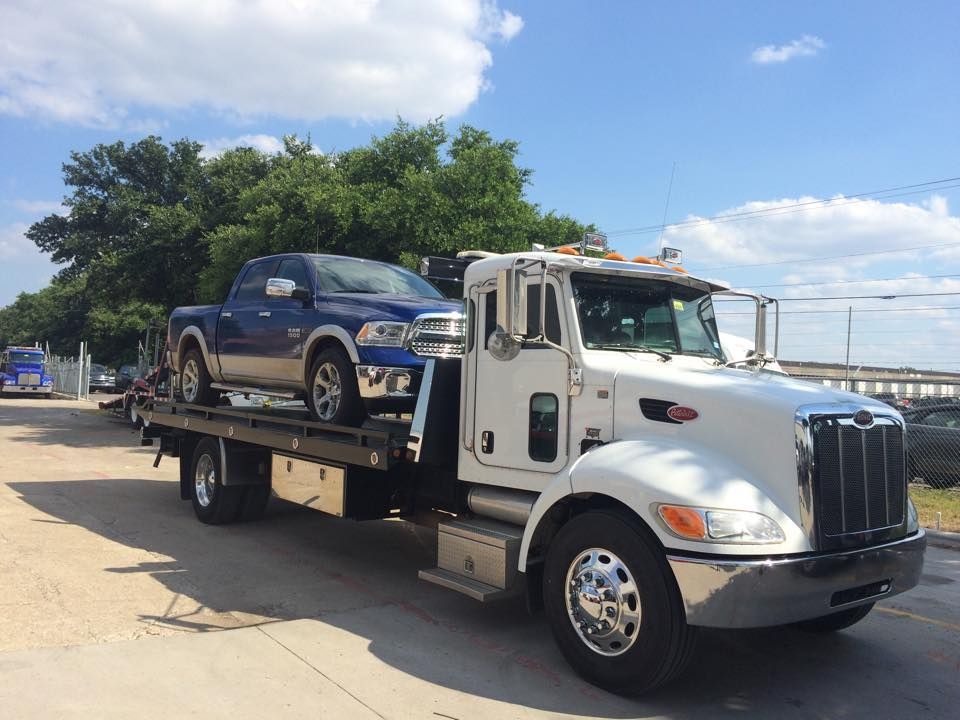 Tow truck carrying a blue SUV on a flatbed under a partly cloudy sky