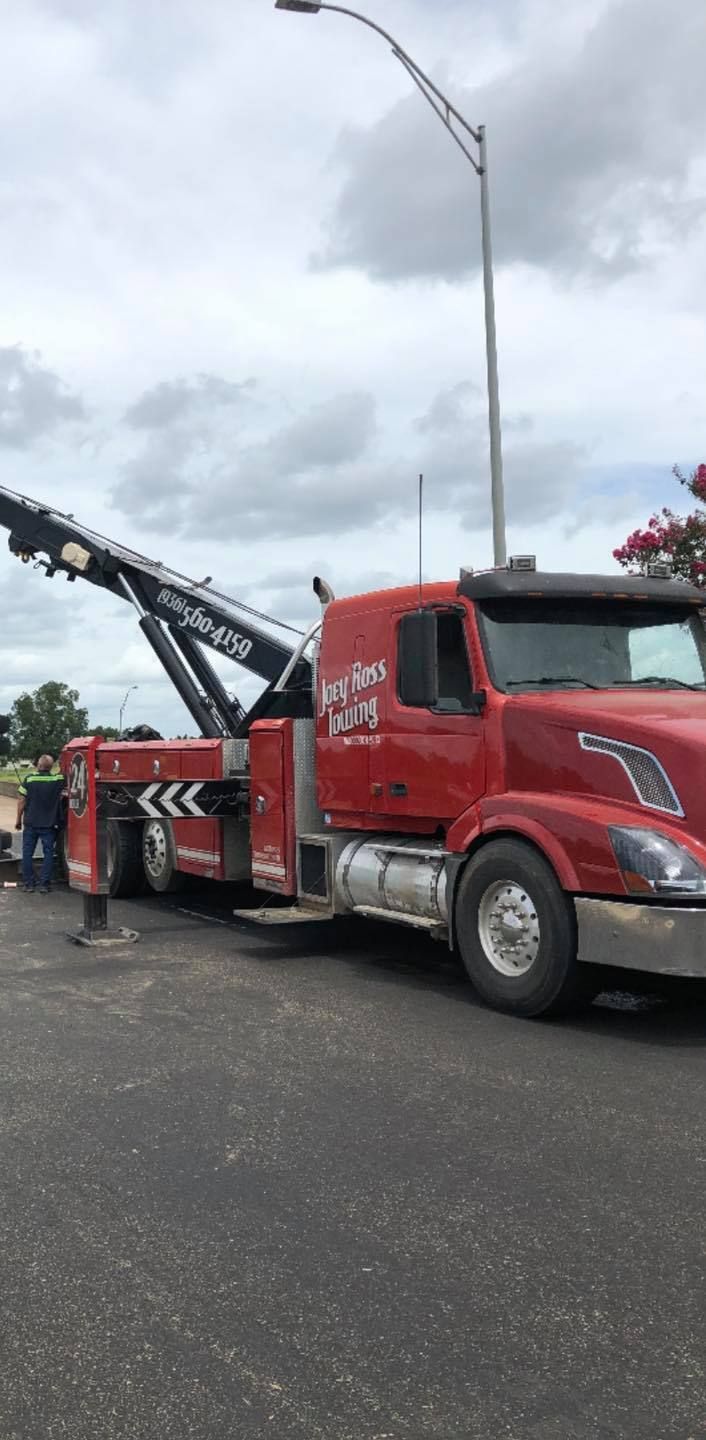 Red tow truck with extended crane parked on a wet road under cloudy sky