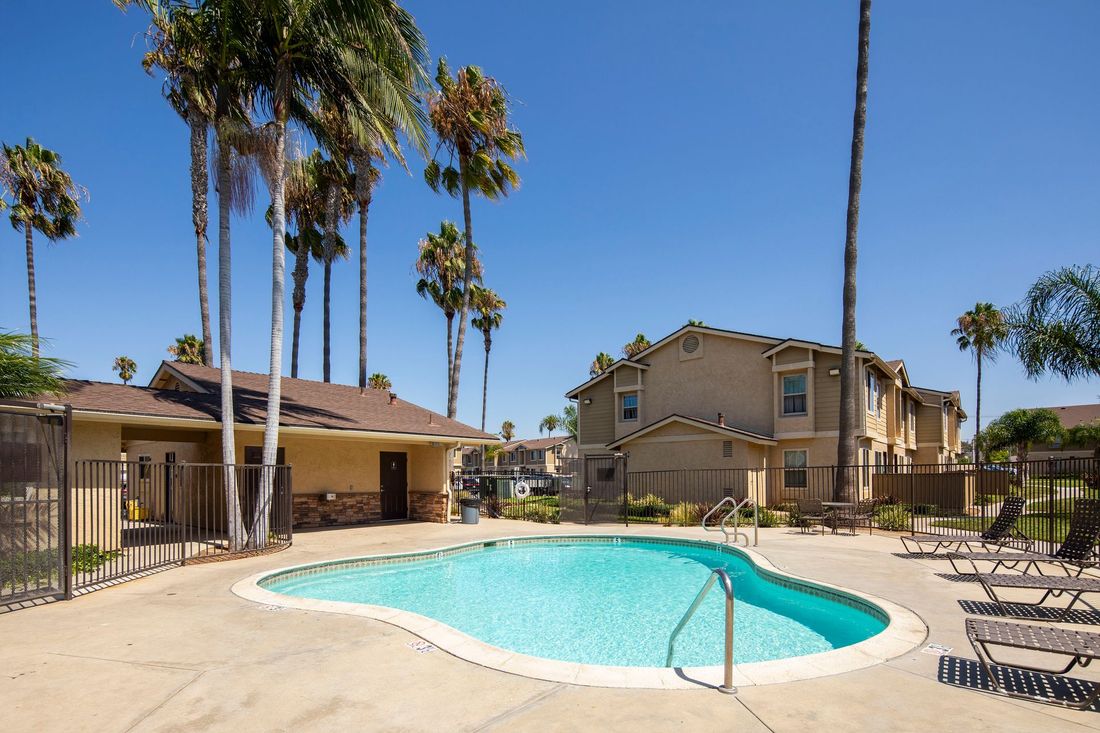 a large swimming pool is surrounded by a fence and palm trees