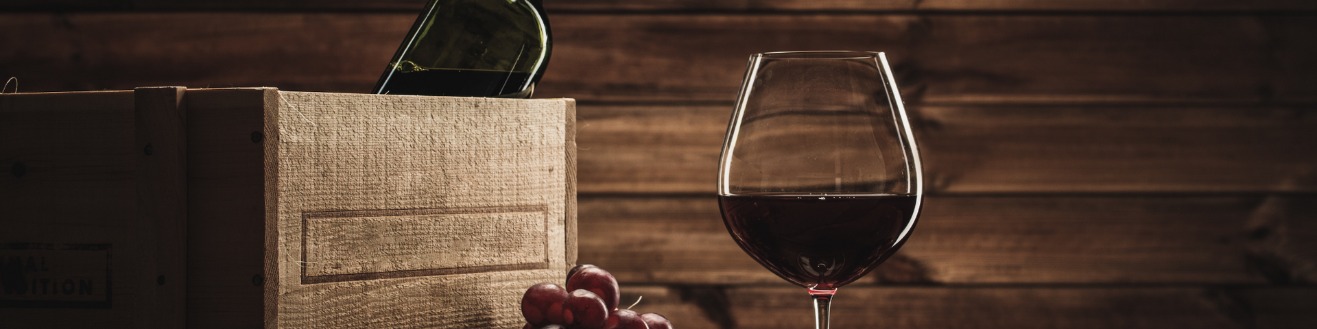 A glass of red wine beside a woven basket on a wooden table, with a rustic wood wall background