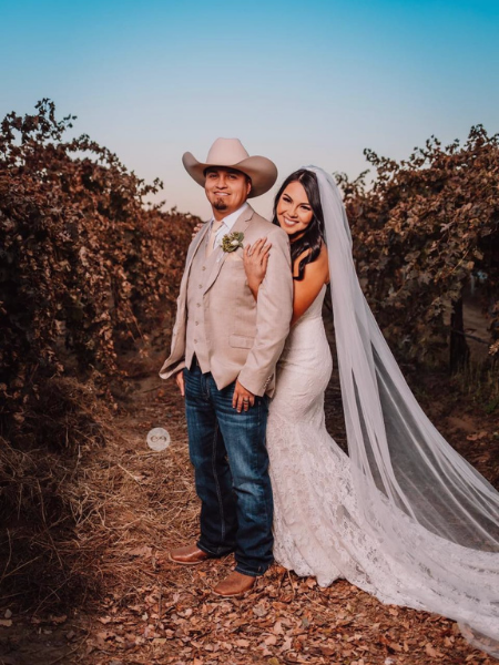 Couple in cowboy hat and wedding dress posing on a vineyard path at sunset