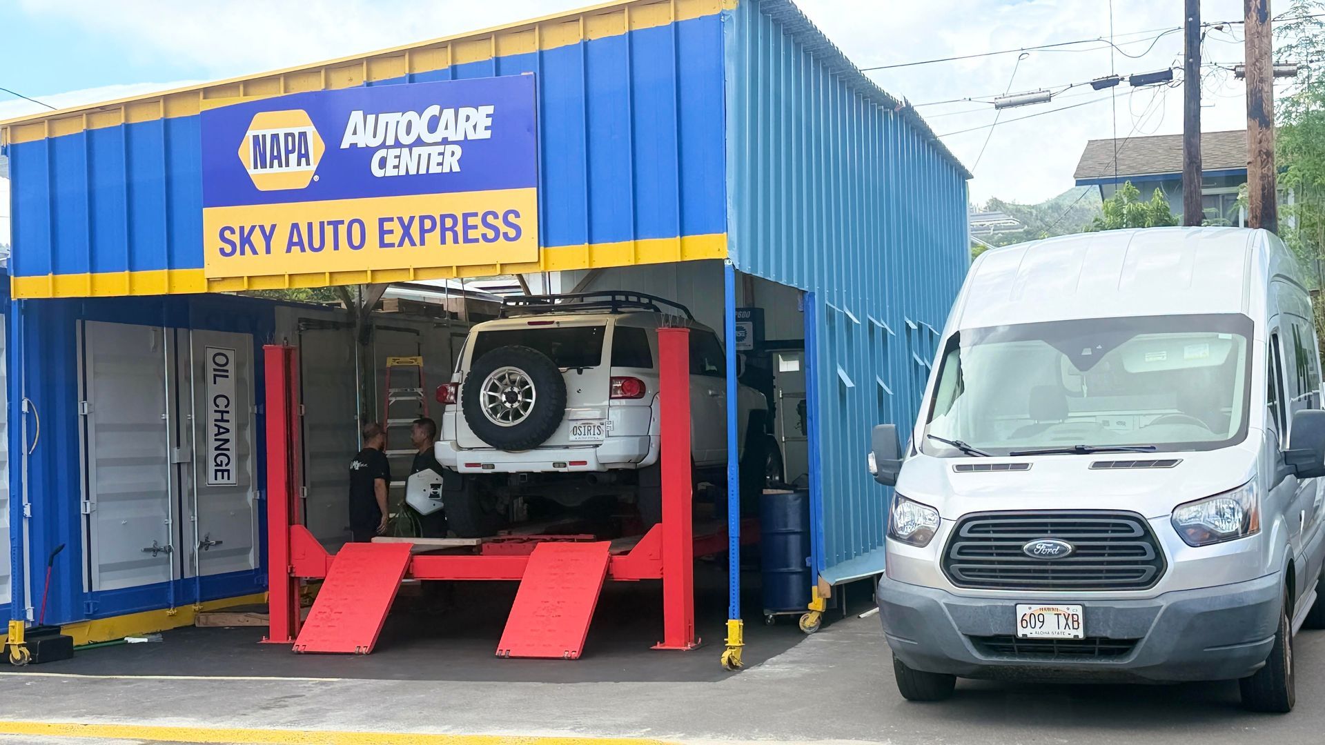 Auto service bay with a white SUV on a red lift and a silver van parked beside it | Sky Auto Repair
