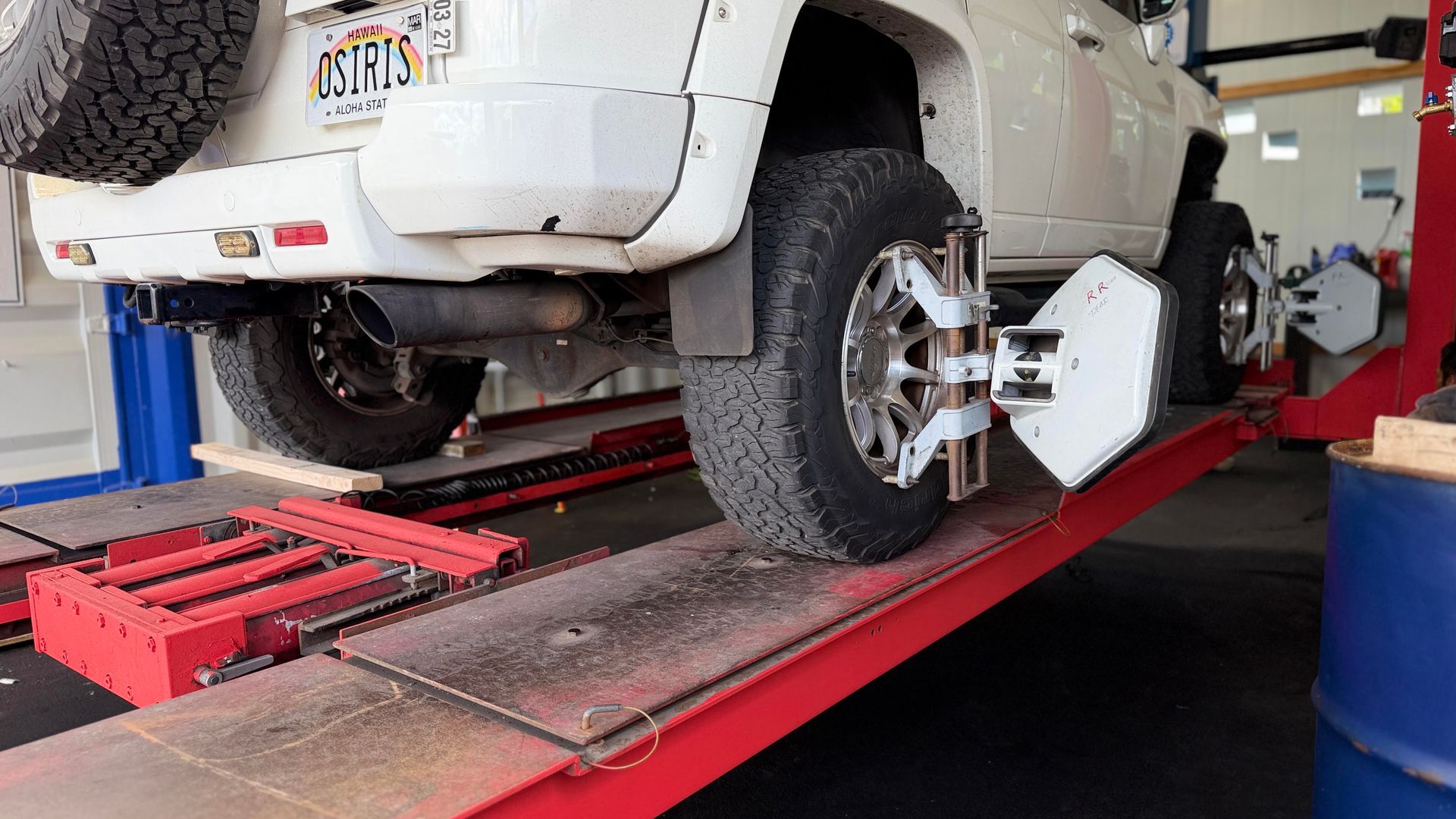 White SUV on a red auto lift in a mechanic’s garage, with a wheel alignment machine attached | Sky Auto Repair