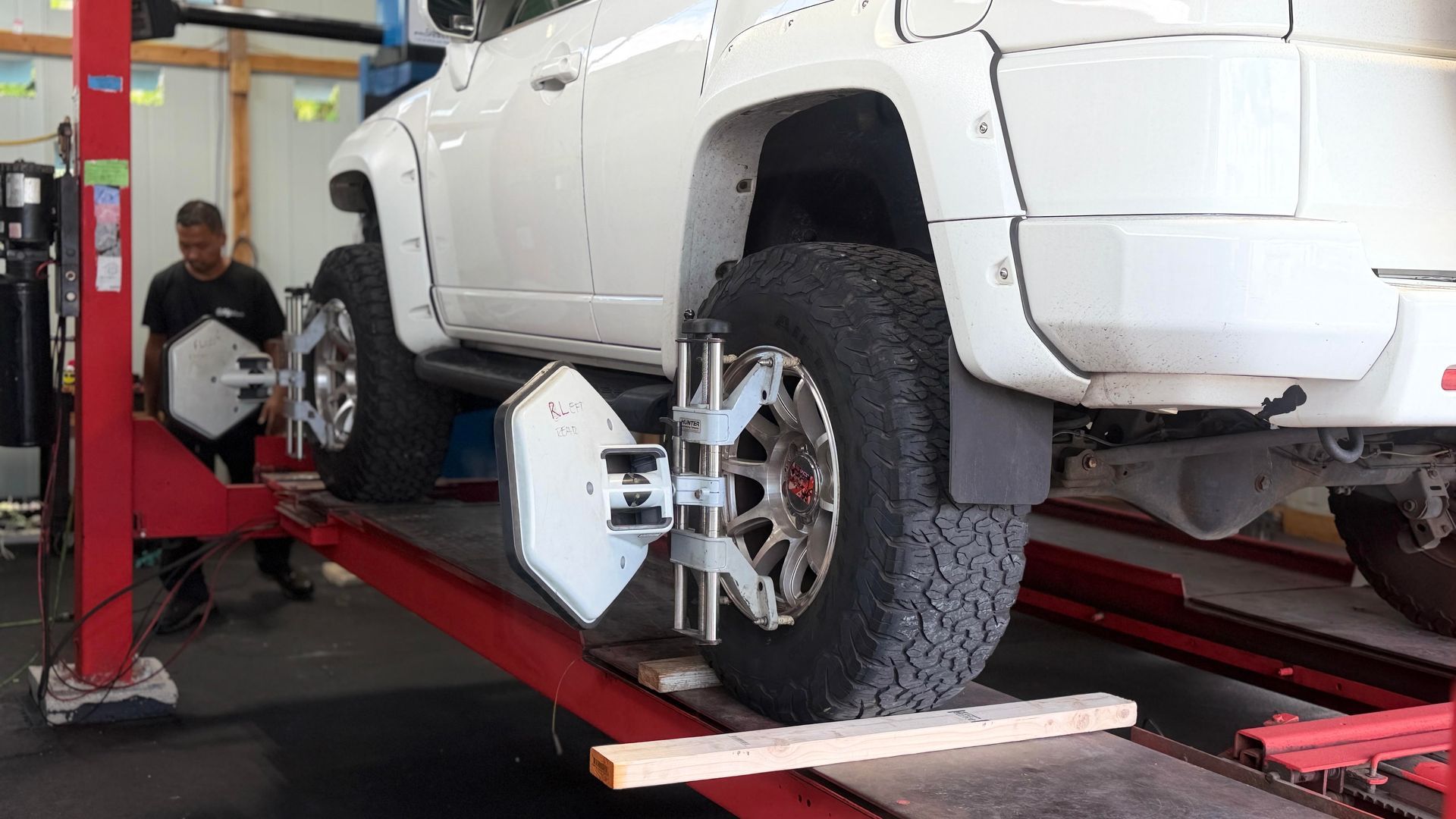 White SUV on alignment lift in auto shop, with mechanic working nearby | Sky Auto Repair