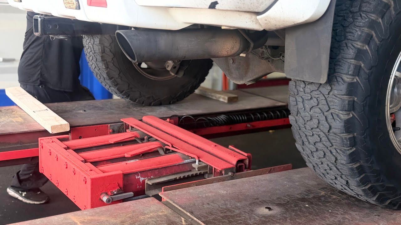 Red hydraulic floor jack lifting a white SUV in a garage, with a wheel removed | Sky Auto Repair