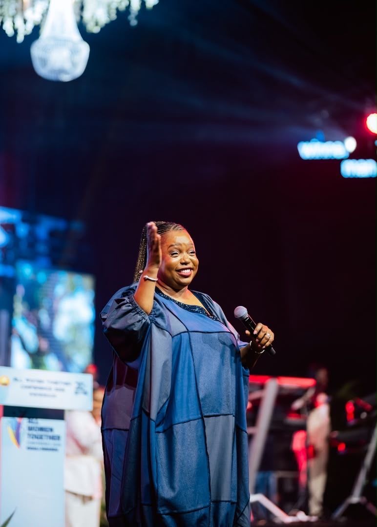 Chevelle Franklyn in a blue dress holding a microphone at All Women Together 2026, Kigali.