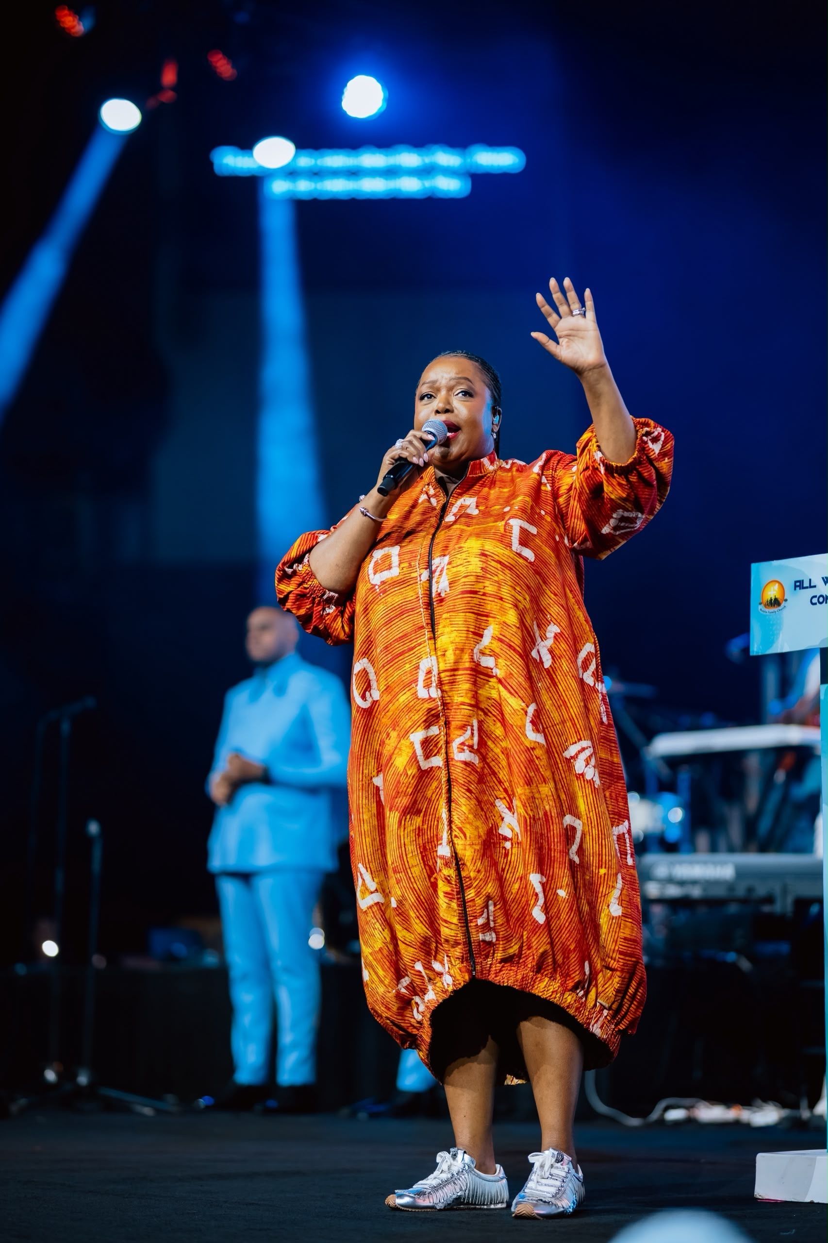 Chevelle Franklyn singing in an orange dress with one hand raised at All Women Together 2026, Kigali.