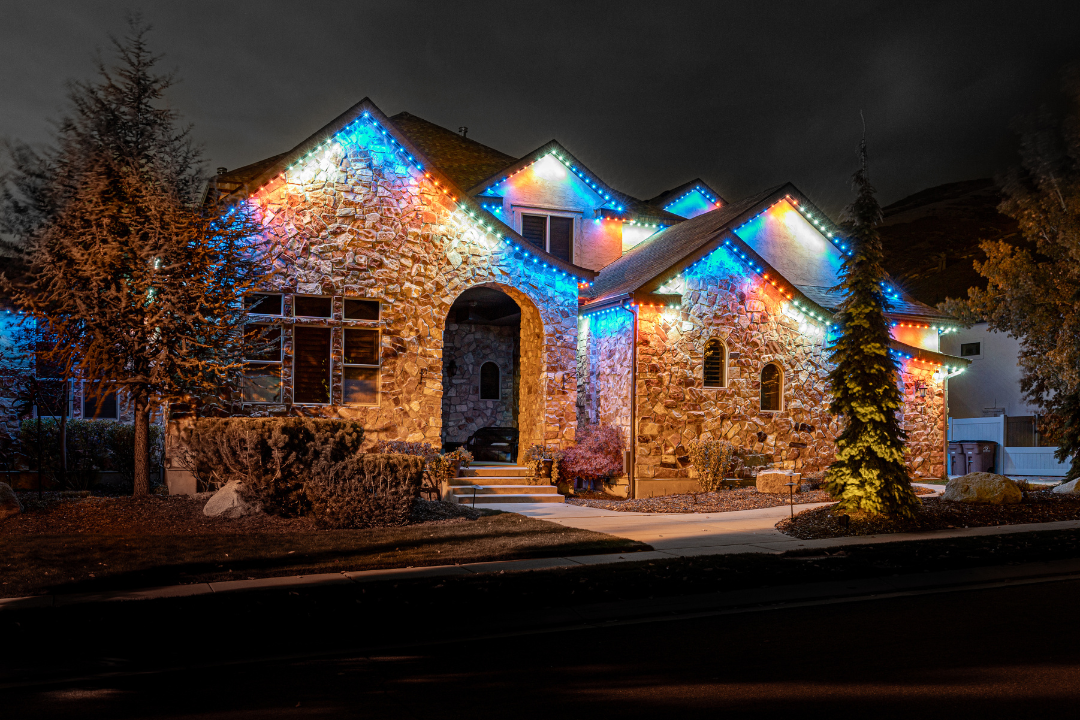 House with stone facade lit with colorful Christmas lights at night.