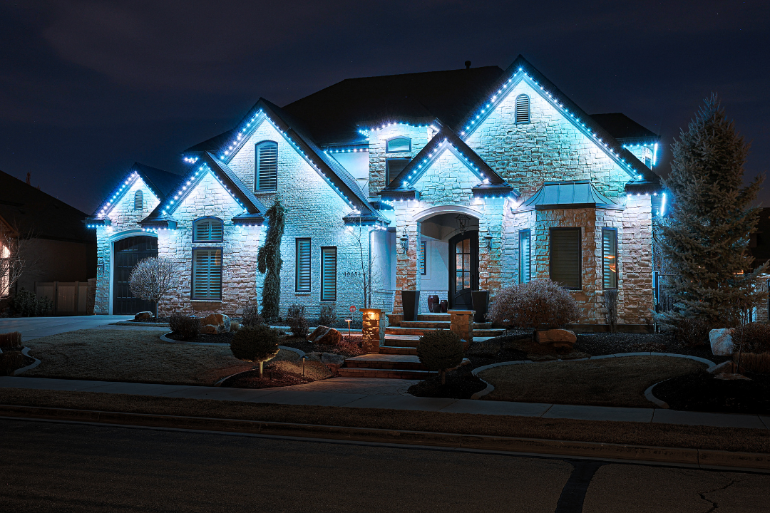 House with blue holiday lights outlining roof and architectural features at night.