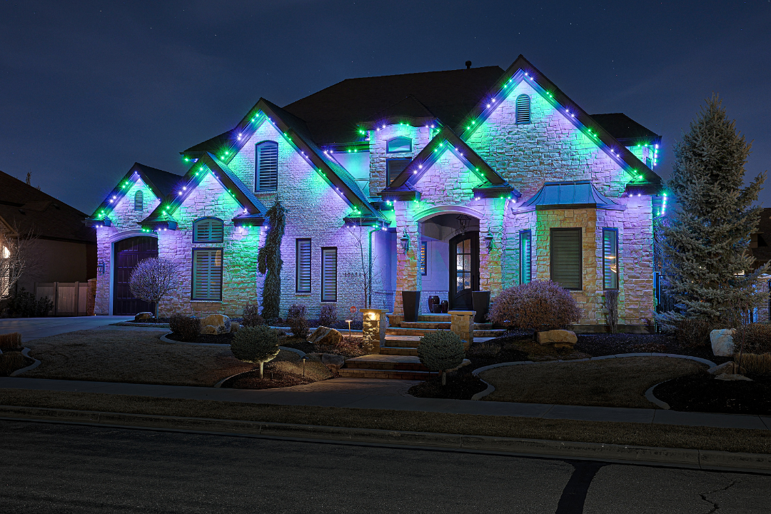 House decorated with colorful Christmas lights at night, glowing blue, green, and purple.