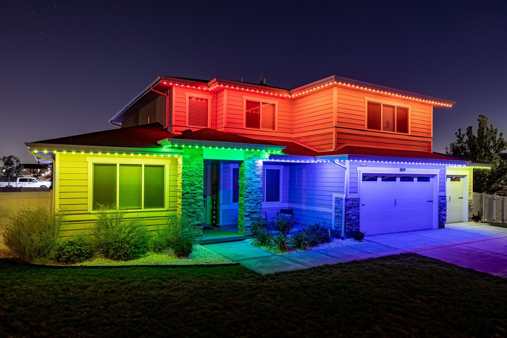 A house illuminated with rainbow-colored lights along the roof and trim against a dark sky.