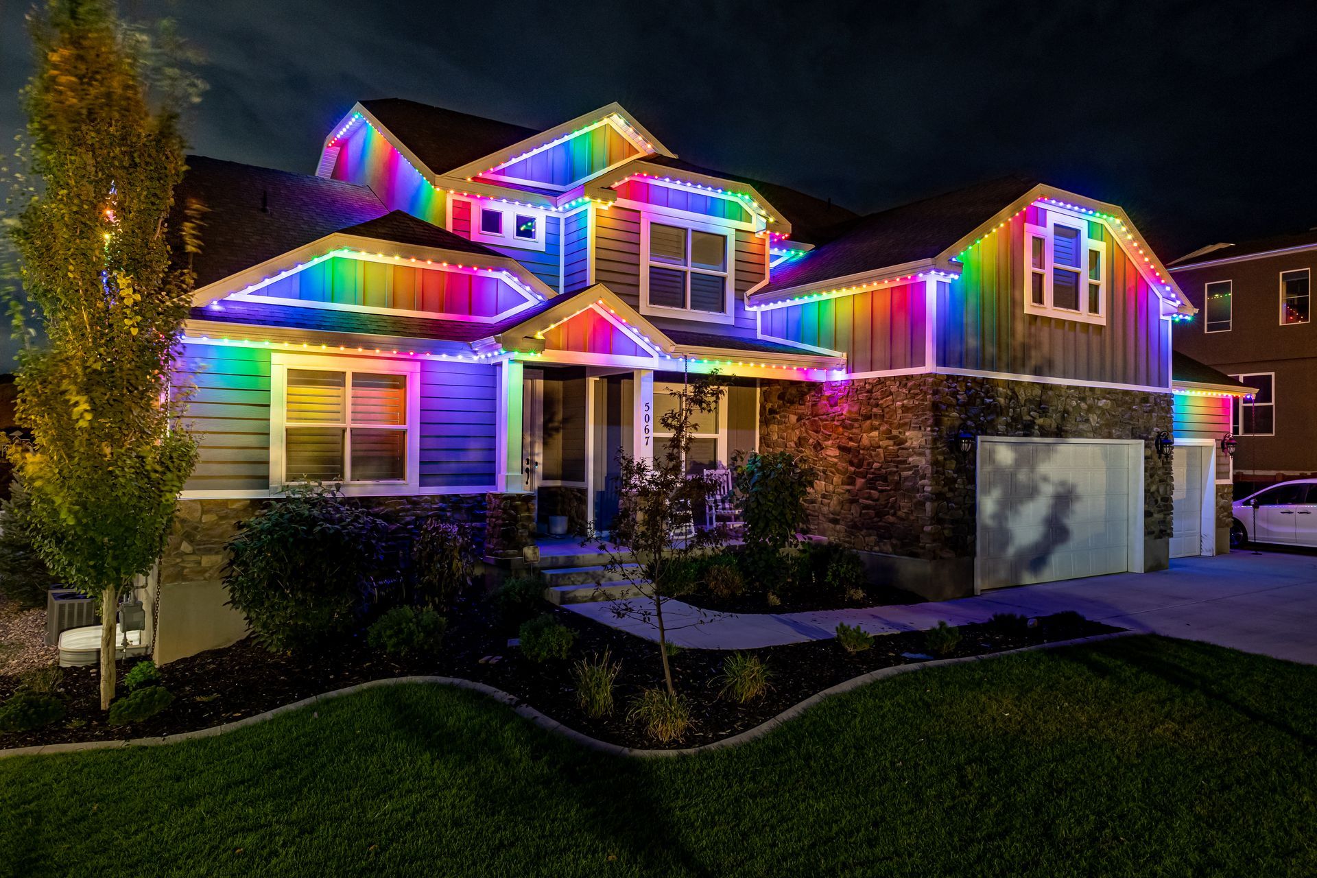 House at night, illuminated with rainbow-colored lights outlining the roof, windows, and trim.